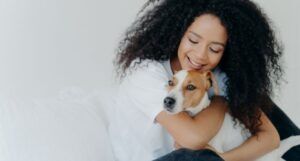 a light-skinned Black woman with voluminous hair is smiling and holding a dog