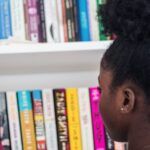 a young Black girl looking for a new book to pick from a bookshelf