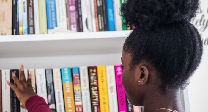 a young Black girl looking for a new book to pick from a bookshelf