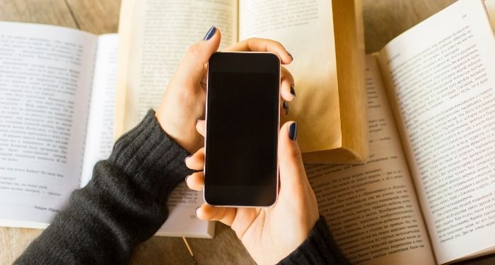 hands holding a black mobile phone over three open books