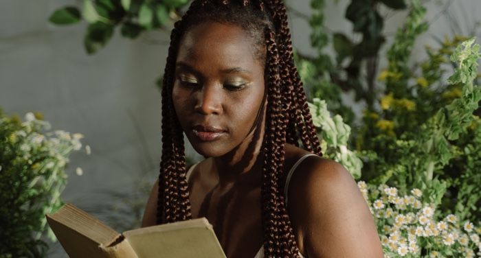 dark-skinned Black woman with brown braids reading a book with plants in the background