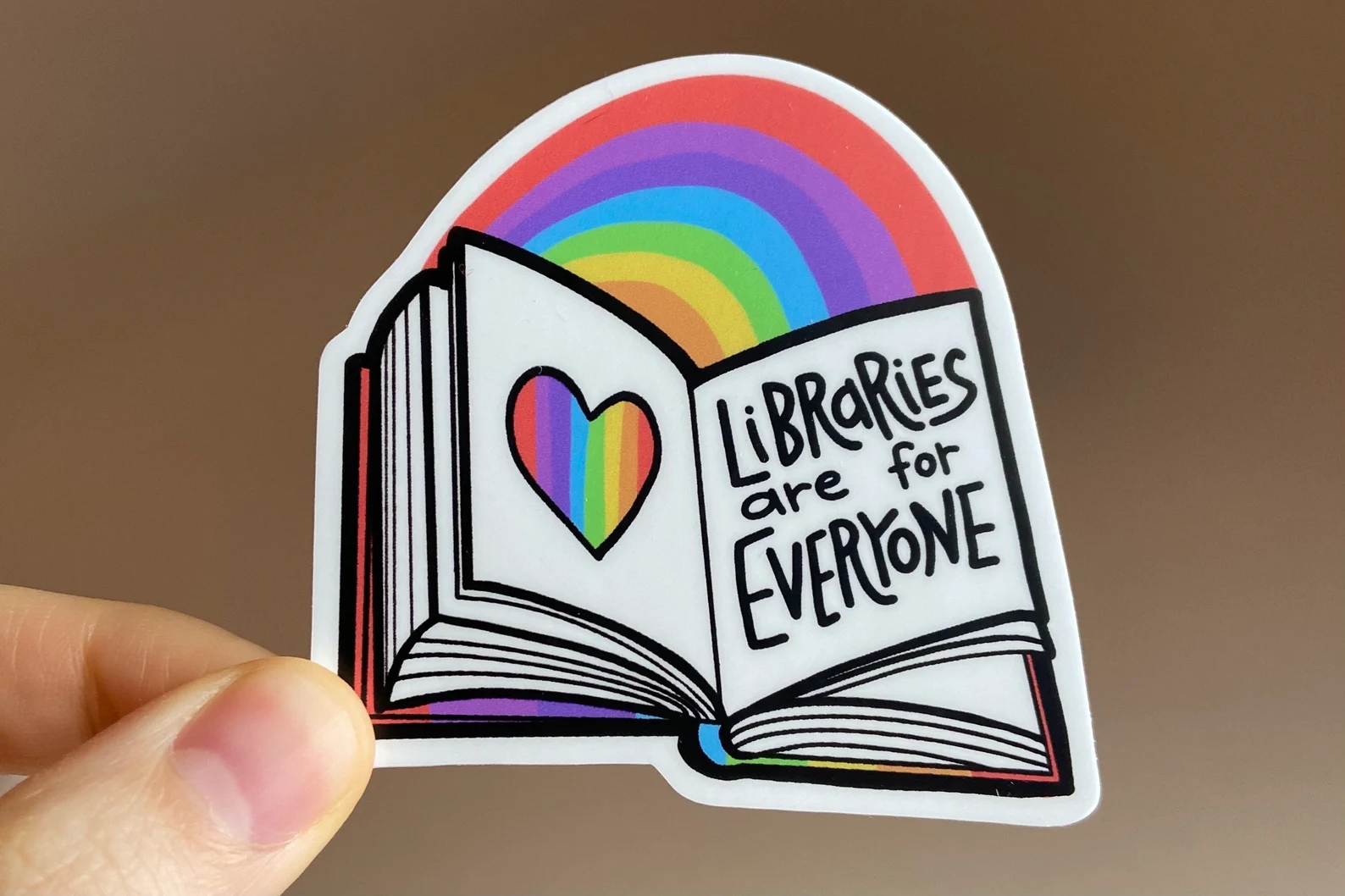 Image of an open book with a rainbow above it. The book page says "libraries are for everyone."