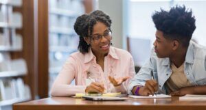 an older Black woman speaking to a Black teen in a library