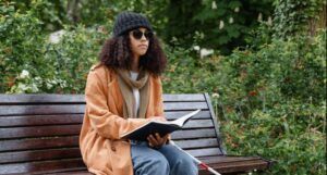light-skinned Black woman reading braille on a park bench