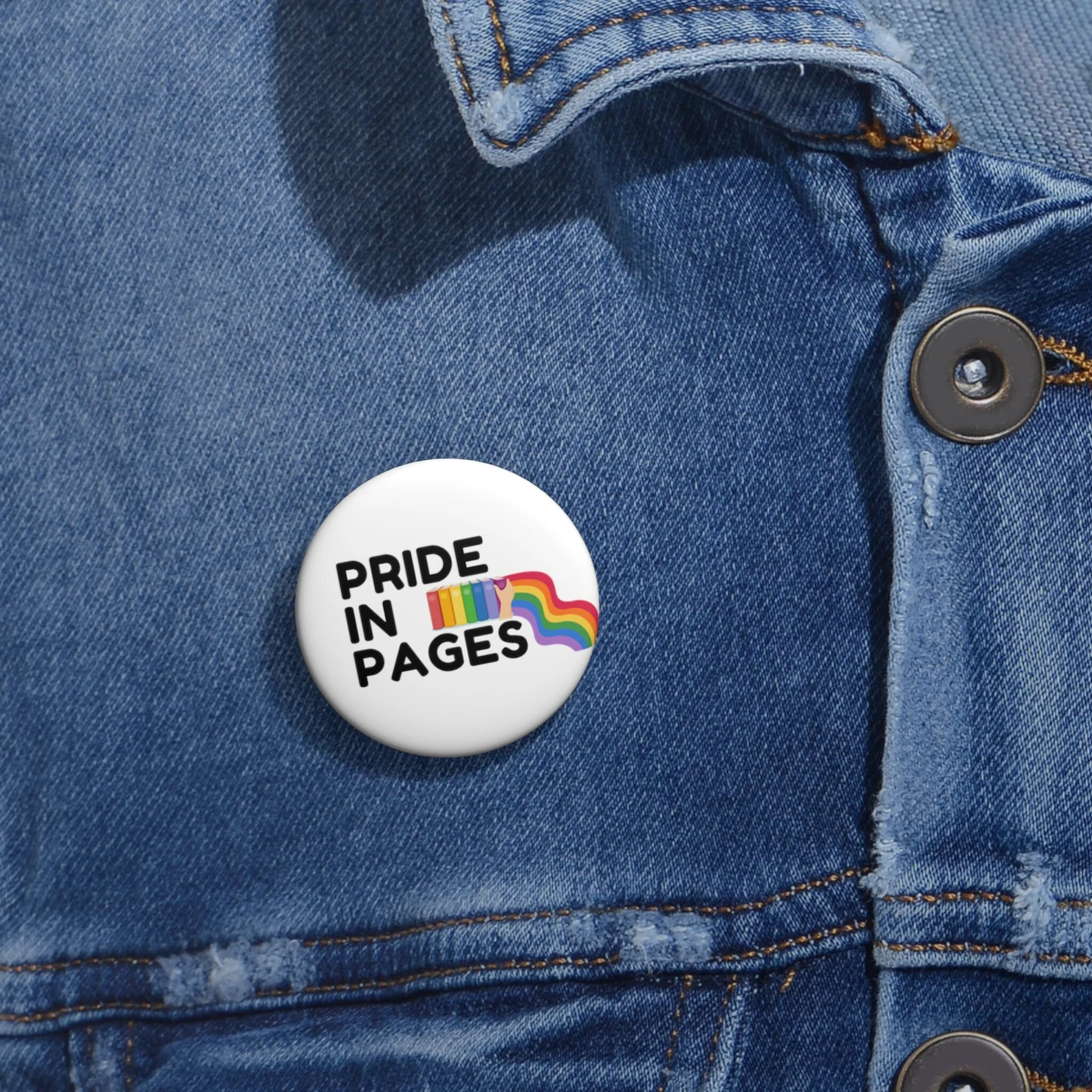 Image of a white button with a rainbow book stack. It says "pride in pages."