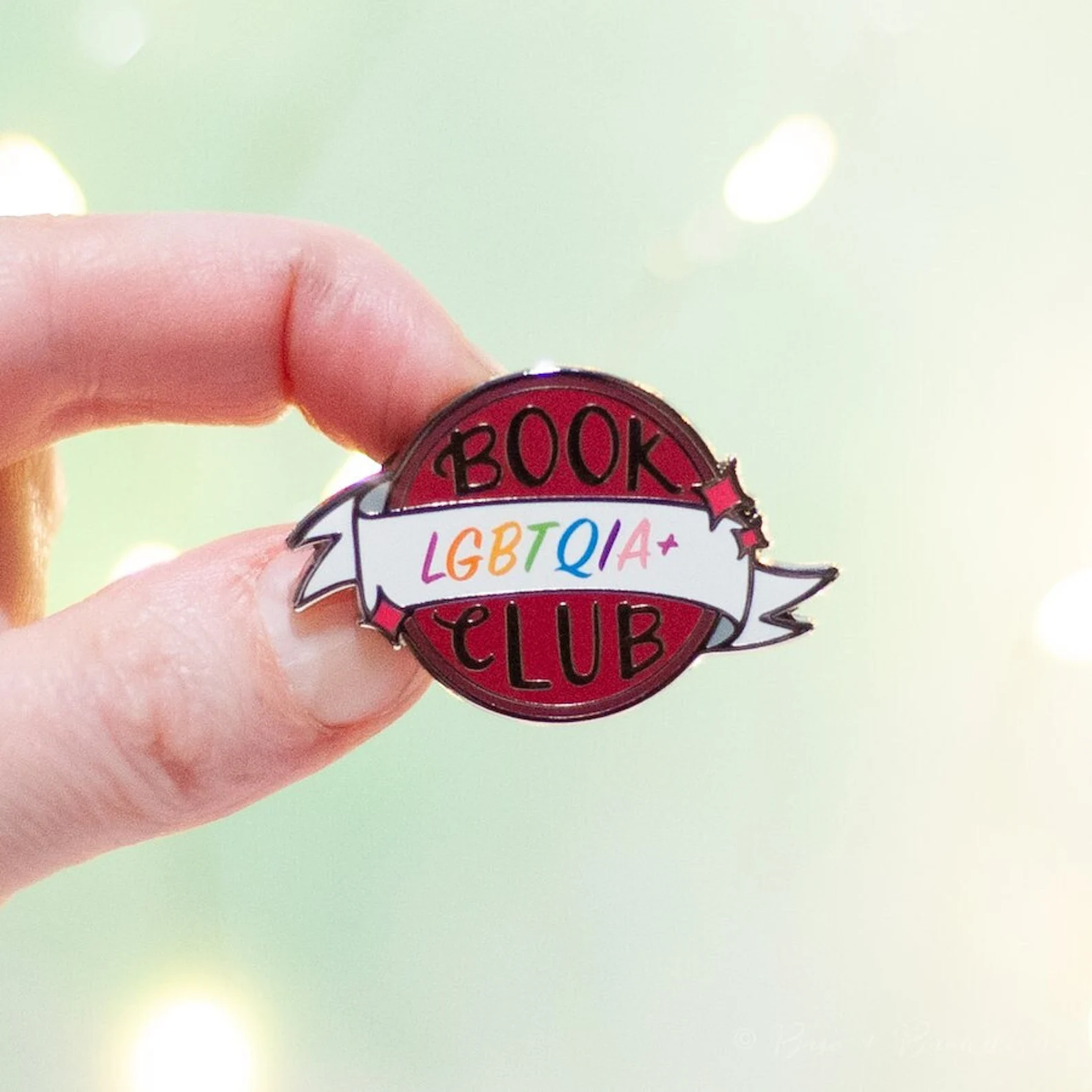 Image of a circle enamel pin that says "LGBTQIA+ Book Club."