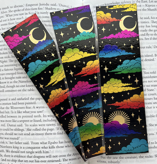 a black bookmark with clouds, moons, and suns in rainbow and gold foil