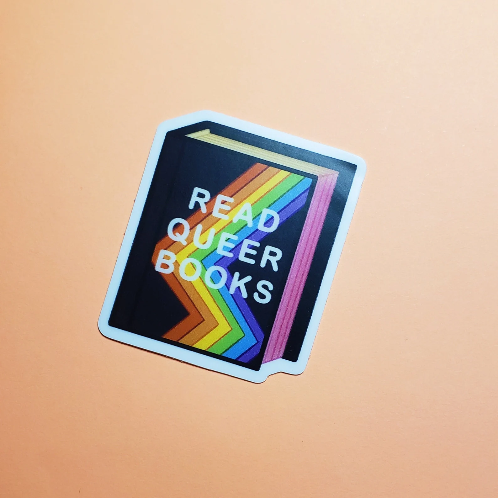 Image of a black book with a rainbow on the cover. It says "read queer books."