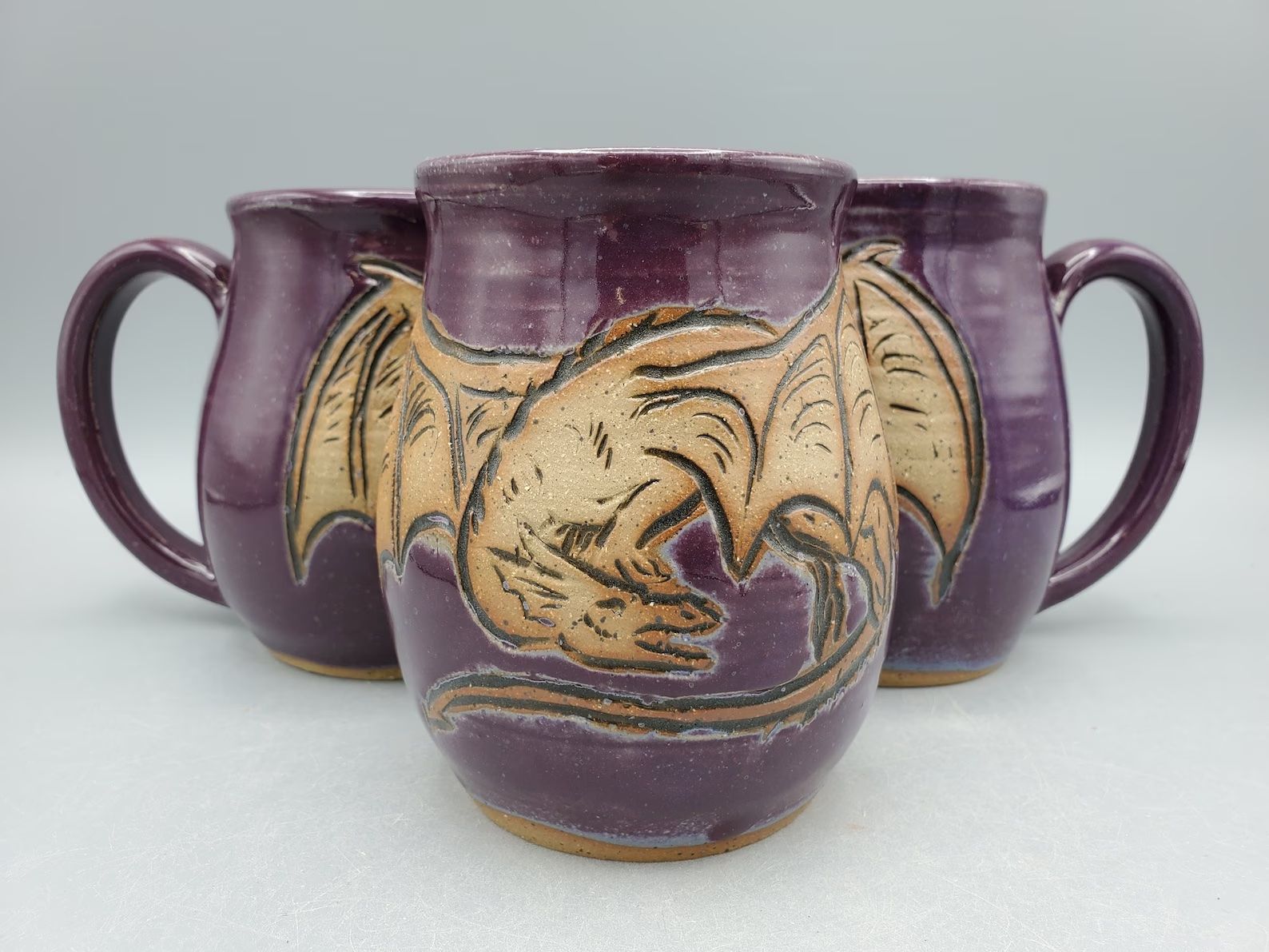 Three purple mugs set in a triangle to form a single dragon sit on a white background. 