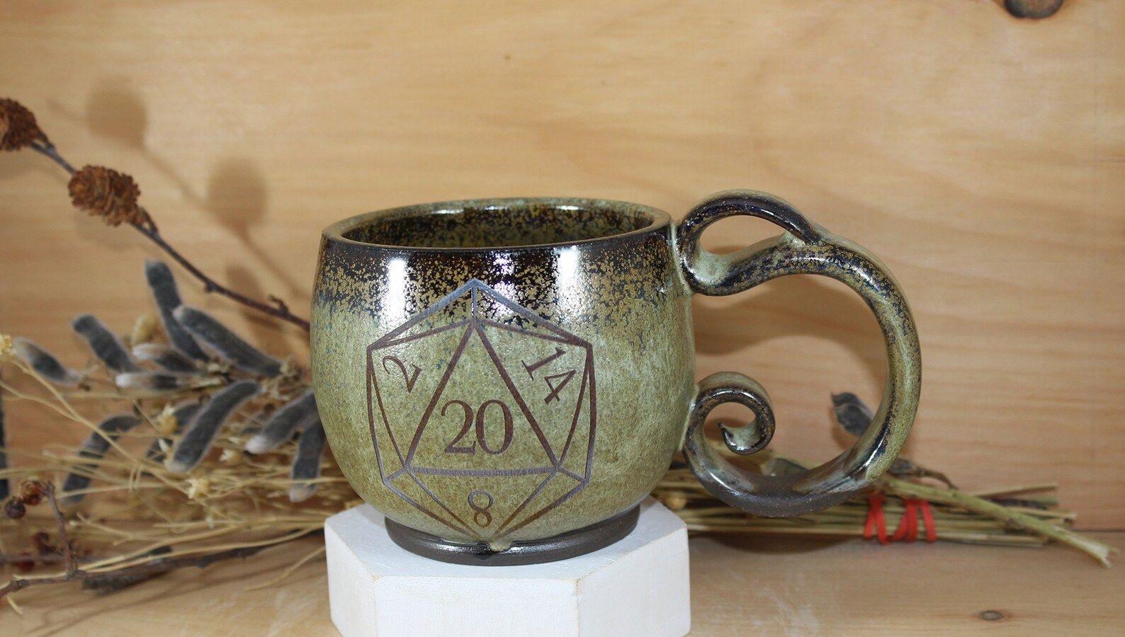 Handmade Green Ceramic 12 oz. D20 Spiral Handle Mug in front of a wooden background with sticks. 