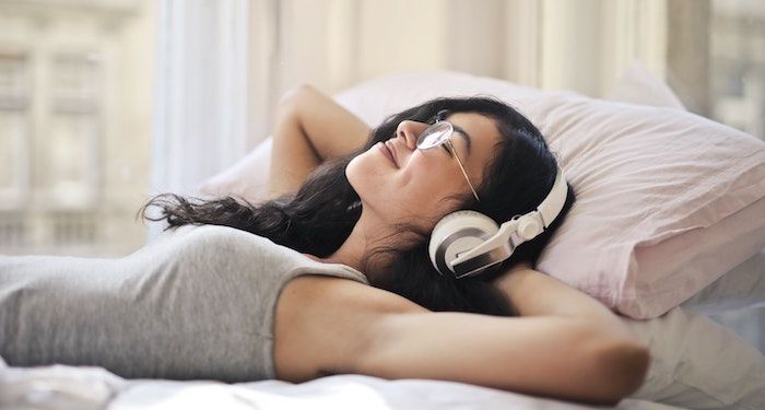 a photo of a woman lying in bed with her arms behind her head, smiling. She's wearing headphones