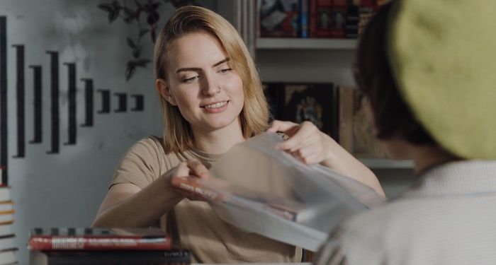 a photo of a bookseller putting a book in a bag for a customer