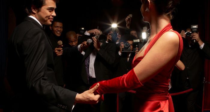 a man in a tuxedo and a woman in a red satin dress holding hands as they're photographed by paparazzi