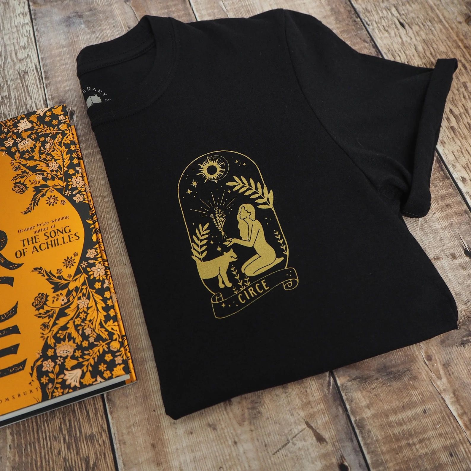 black tshirt with yellow drawing of a woman kneeling before a lion and holding up a bouquet of flowers