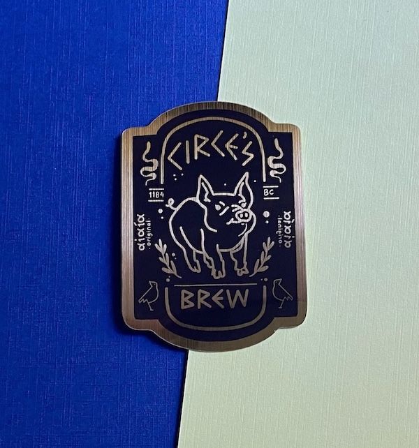 blue and silver pin with a line drawing of a pig and the words "circe's brew"