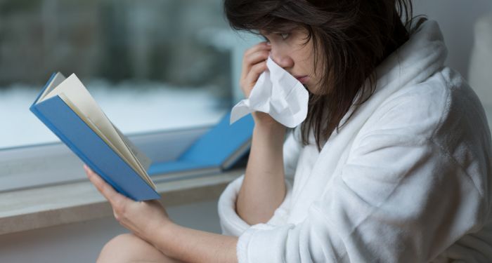 woman crying and holding a tissue to her face while reading a book