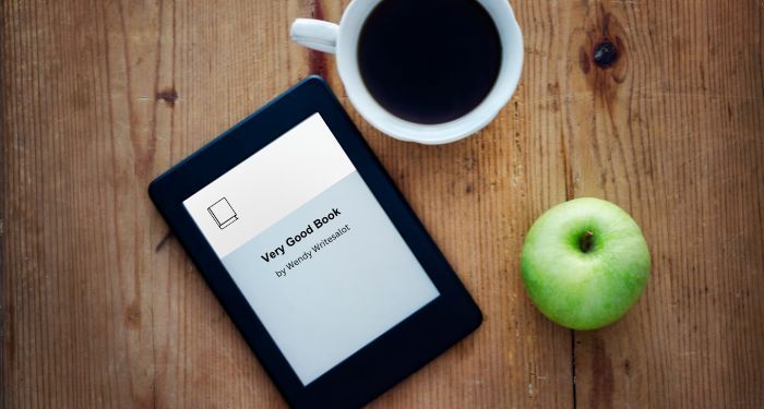 an ereader, cup of coffee, and a green apple photgraphed from above on a wooden surface