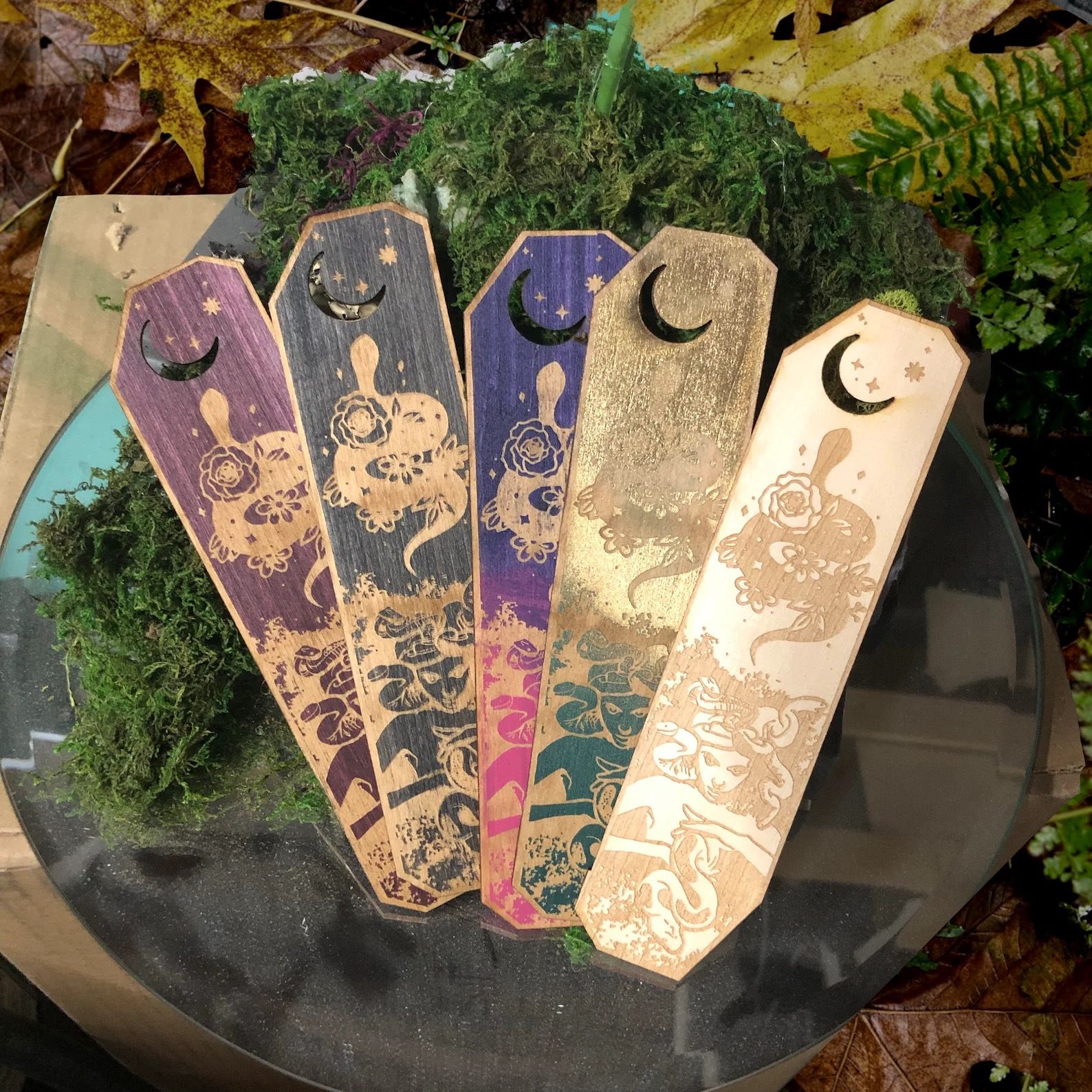 five wooden bookmarks in assorted colors with carved illustrations of a woman with serpents for hair at the bottom and a serpent adorned with roses at the top 