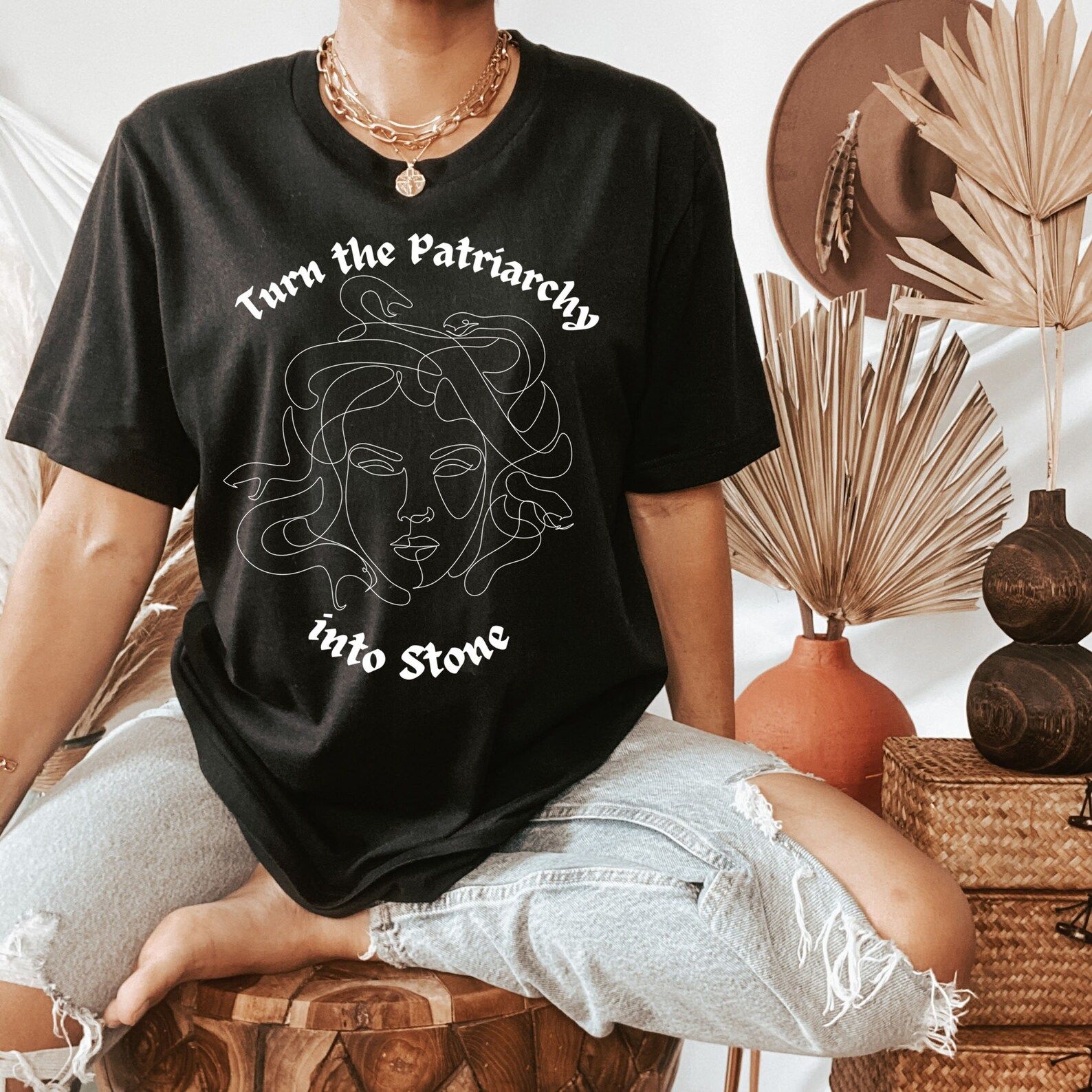 torso of a person wearing a black tshirt with a white line drawing of medusa and text that reads "turn the patriarchy into stone"