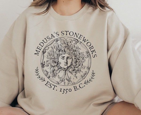 taupe-colored sweatshirt with a line drawing of Medusa's head and text that reads Medusa's Stoneworks Est 1350 BC