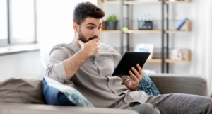 a photo of a man reading on a tablet with eyebrows raised and a hand over his mouth