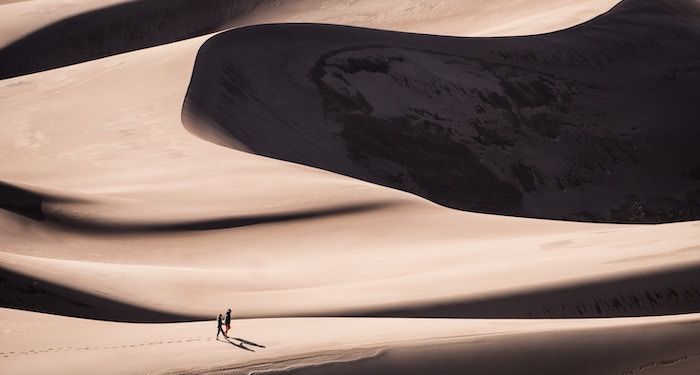 a photo of two small figures walking across giant sand dunes
