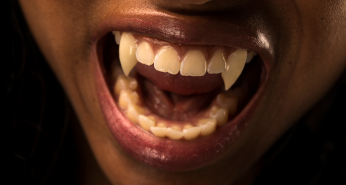 a person with dark skin and vampire teeth baring their teeth