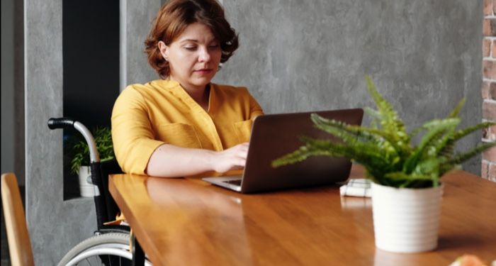 white woman in wheelchair at a table on a laptop