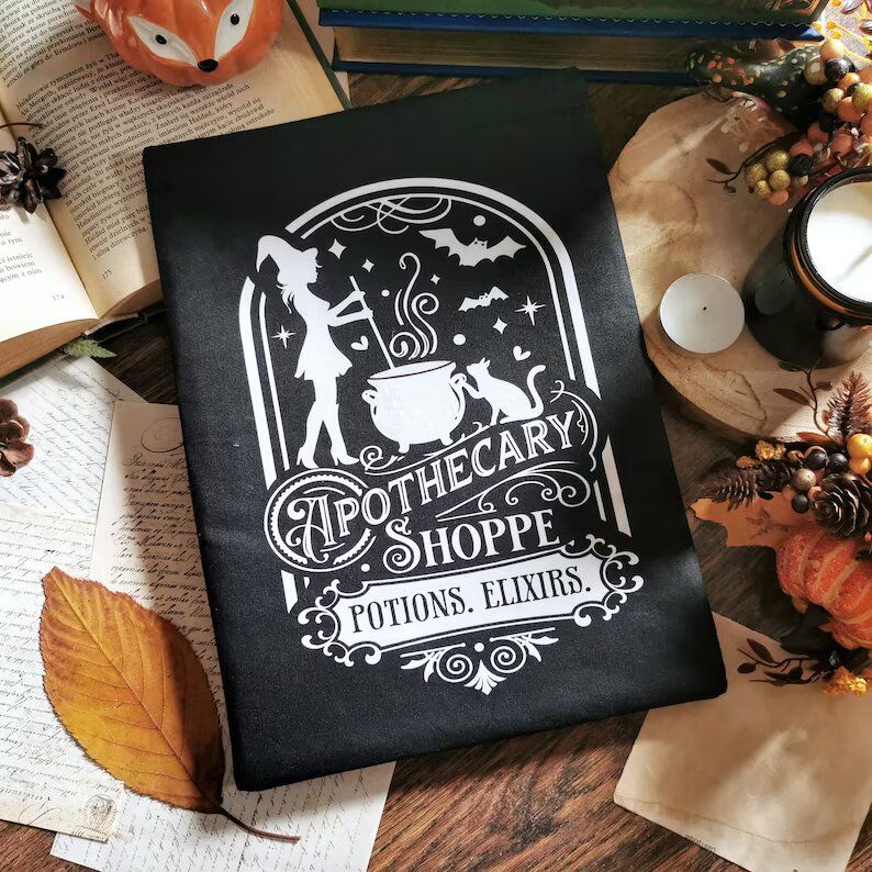 Black book sleeve with an illustration of a witch stirring a cauldron. There are also a cat and bats. Text: Apothecary Shoppe. Potions. Elixirs
