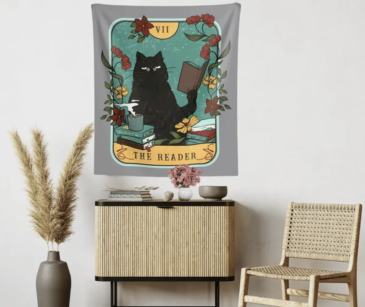 A fabric hanging tapestry designed to look like a tarot card that says "The Reader" with an illustration of a black cat reading a book