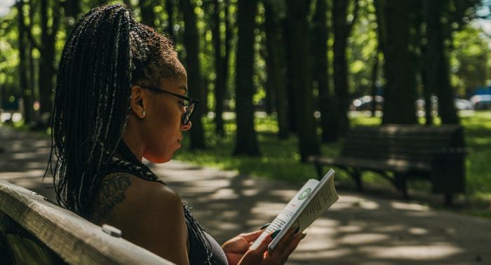 Black woman reading on park bench