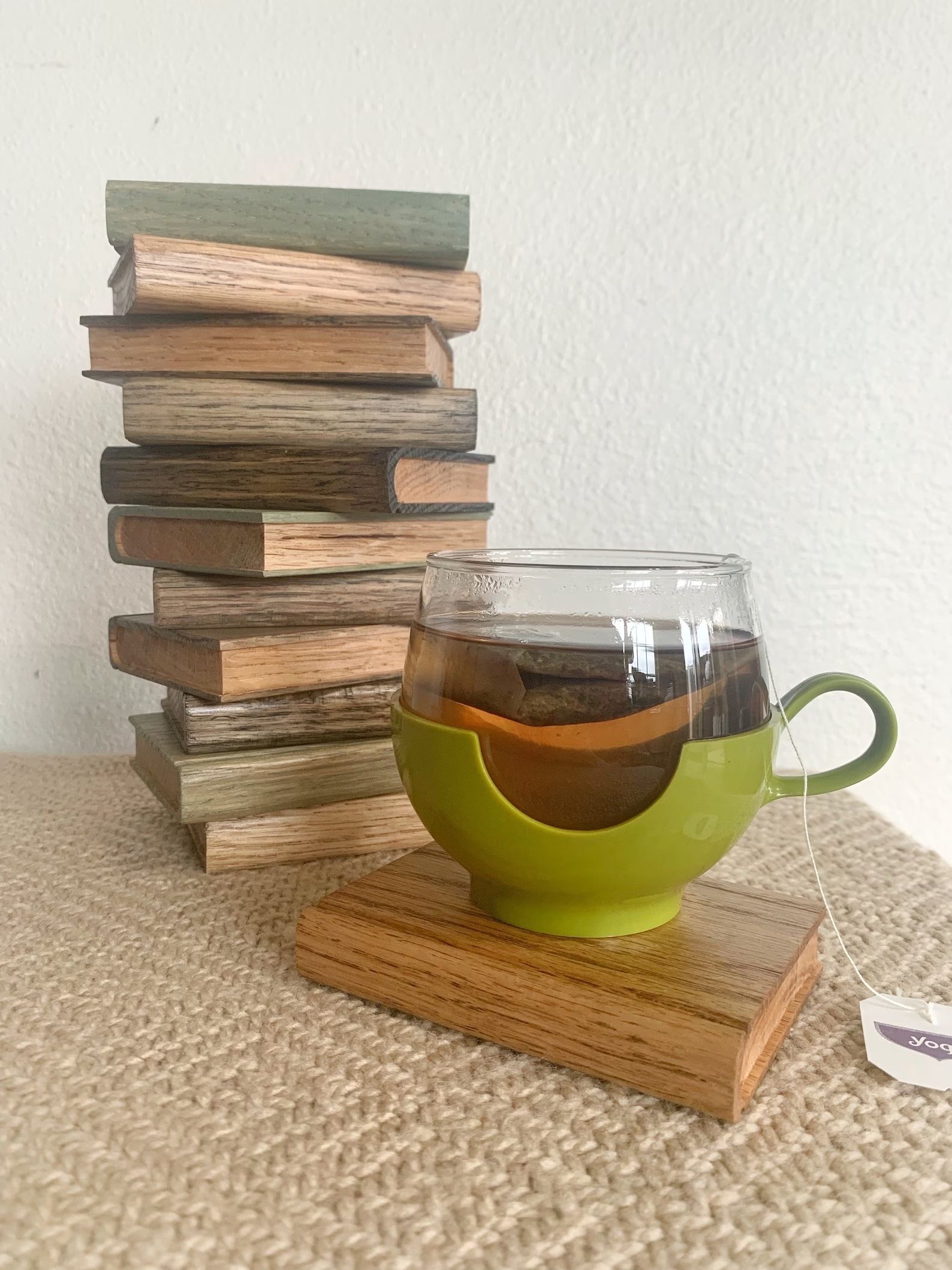 Book shaped wooden coasters in a stack are behind a book shaped wooden coaster with a glass of tea on a table.