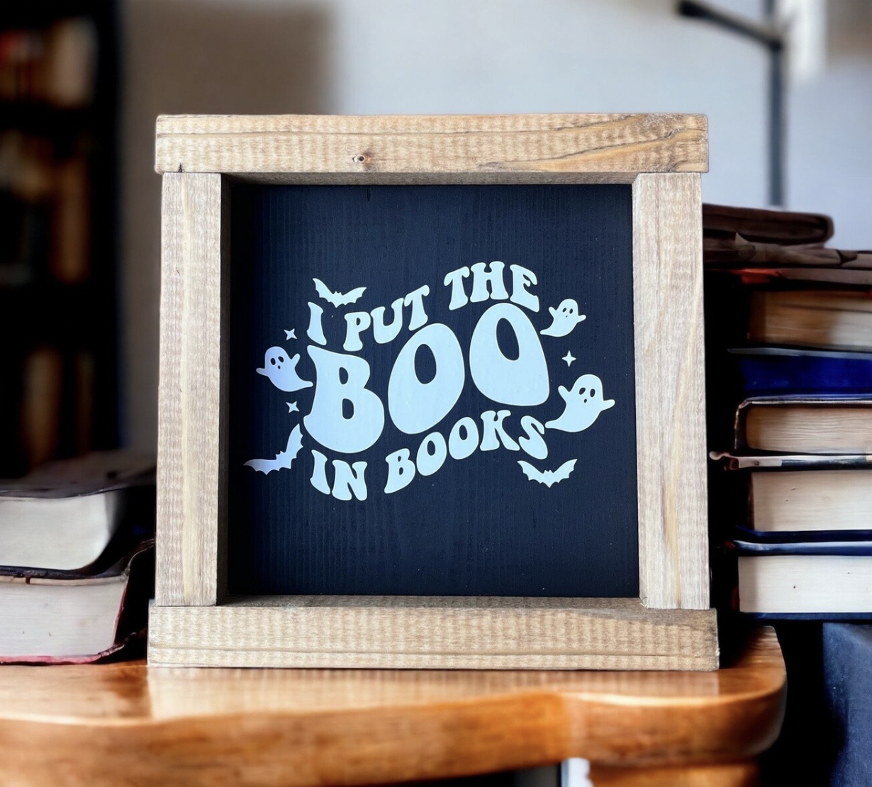 A small black sign with a wooden frame that says "I Put the Boo in Books"
