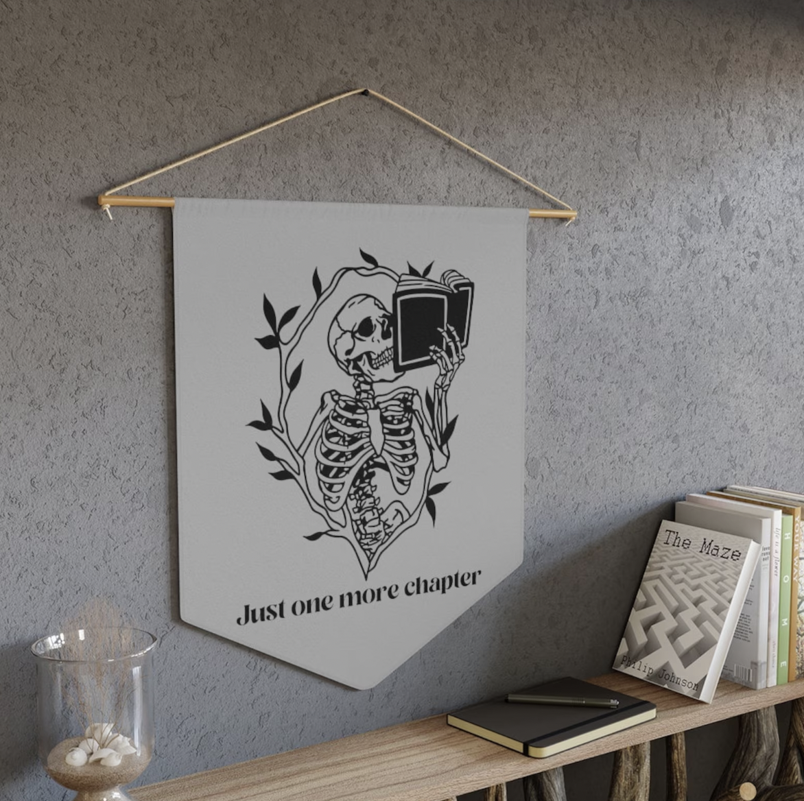 A hanging wall banner with an illustration of a skeleton reading a book and the text "Just one more chapter"