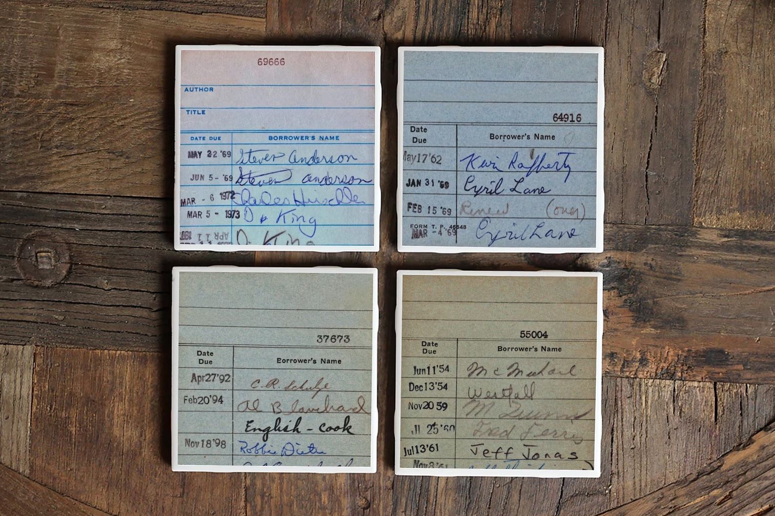 Four ceramic library due date coasters sat on a wooden table.