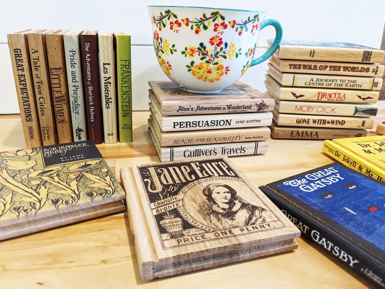 Three stacks of wooden coasters with book titles and covers printed on them are behind three book coasters on a table. 