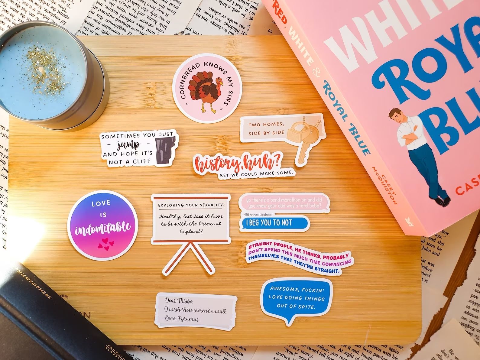 Red White and Royal Blue Matte Vinyl Stickers inspired by Casey McQuiston are on a wooden board with a copy of the book and a candle.