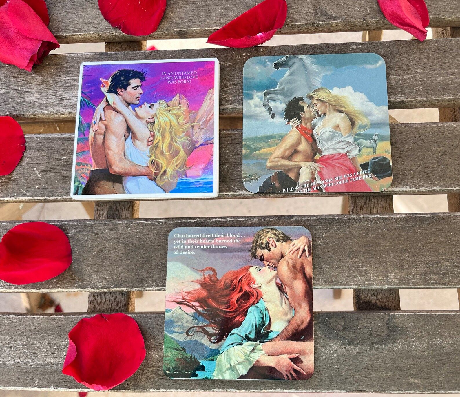 Three coasters with classic romance book covers sit on a wooden table with rose petals.