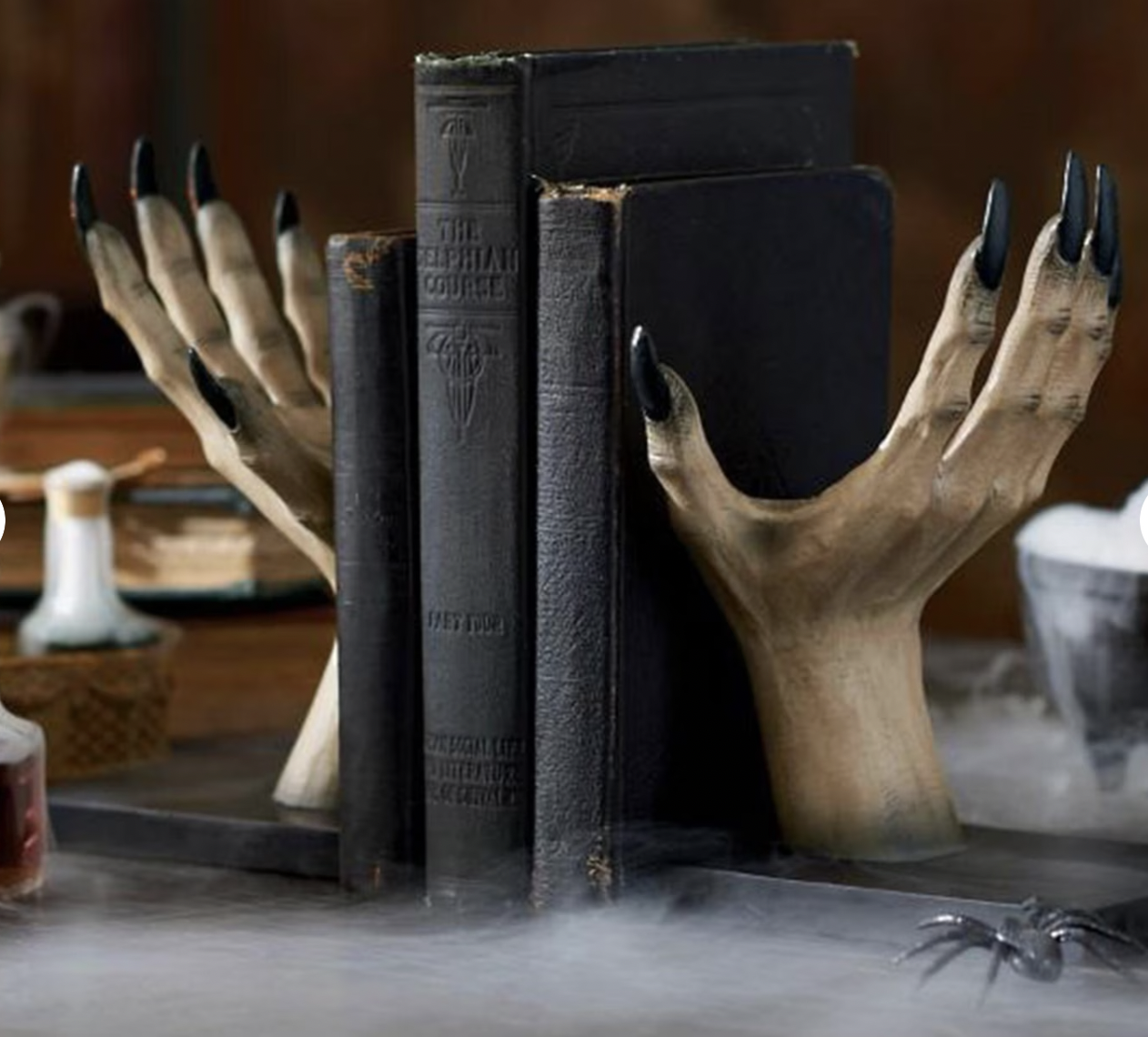 Two fake witchy hands stretched upwards with long black nails hold up three books as bookends