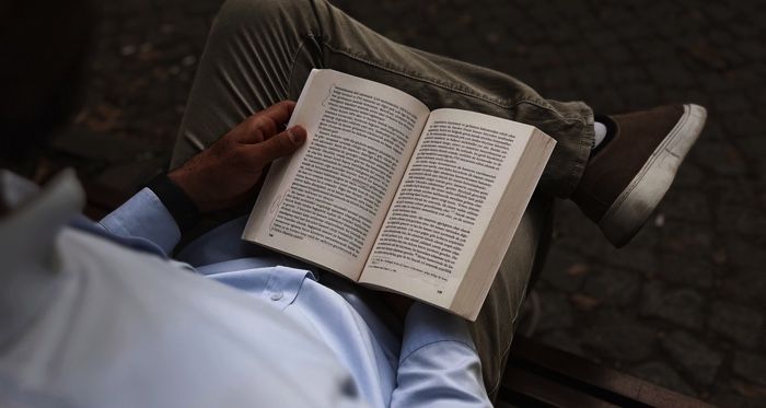 a brown-skinned man sitting on a bench and reading a book