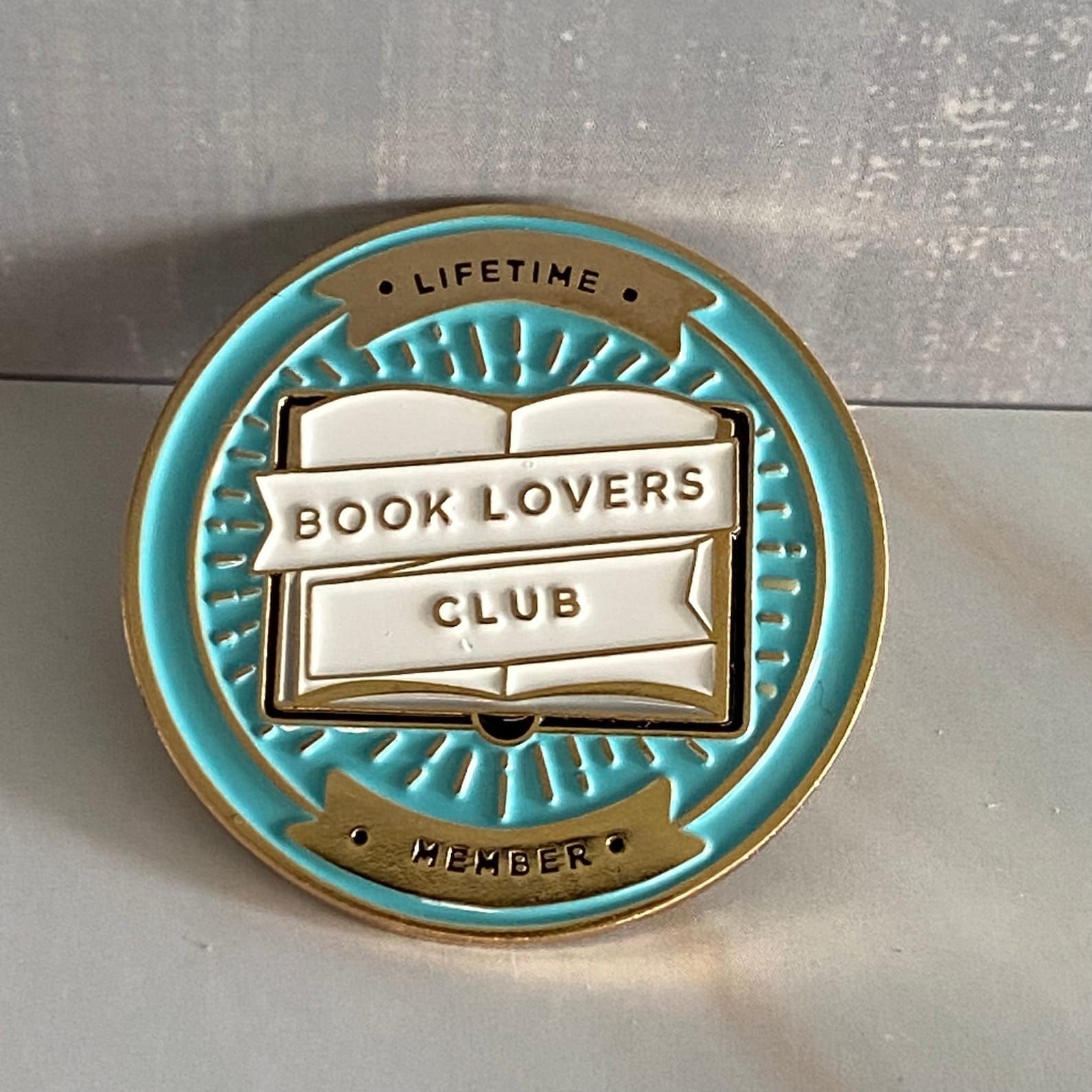 blue and gold pin that reads Book Lovers Club on an open book, and "lifetime membership" on the perimeter of the pin.