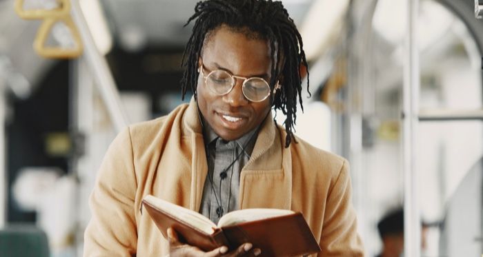 dark brown-skinned Black man with locs reading a book while on public transportation