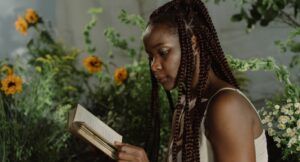 dark brown-skinned woman with braids reads a boot in a lush green garden