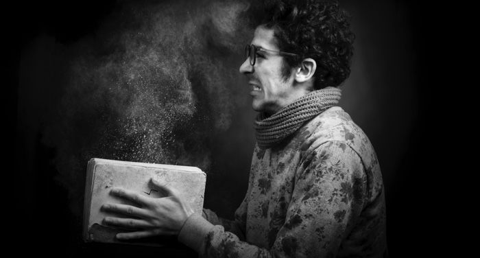 black and white photo of a fair-skinned man with dark, curly hair slamming a book closed and grimacing