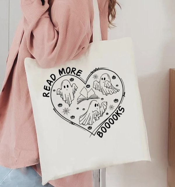beige tote bag with a black screen print of a heart with ghosts inside that says read more boooooooks