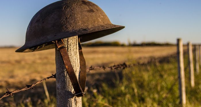a rusted military helmet resting on a post held up by barbed wire