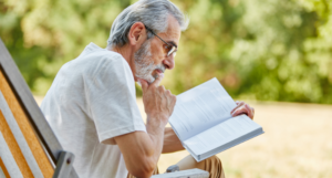 a photo of a man with grey hair reading a book outdoors
