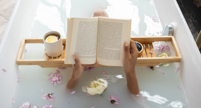 a photo of a person reading in the bath with a bath tray that has a drink and a bowl of berries on it