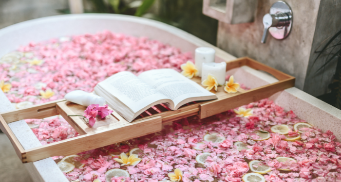 a photo of a bath with flowers and lemon slices. There's a bathtub tray with an open book, candles, and more flowers