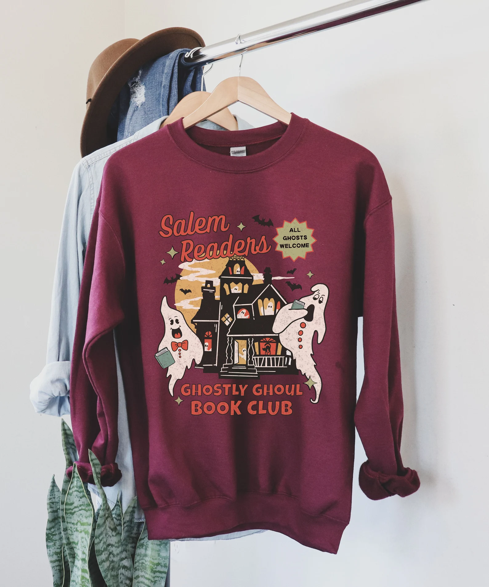 maroon sweatshirt with images of ghosts and a haunted house. it says "salem readers ghostly ghouls book club."